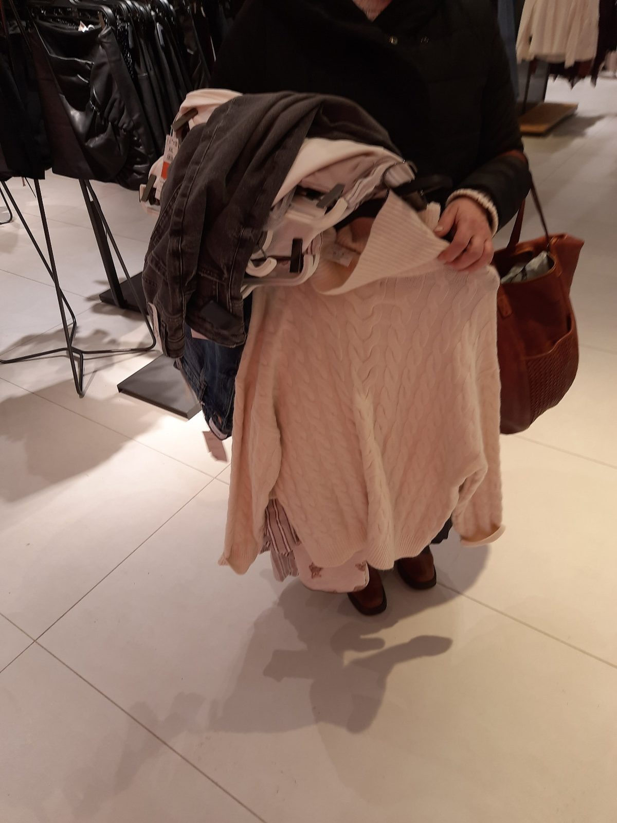 A customer carrying many garments on hangers in her arms