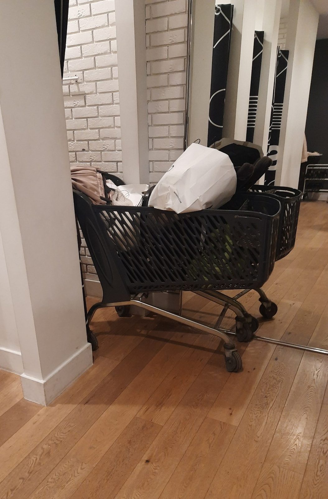 A grocery store trolley full of clothes and bags next to the fitting rooms